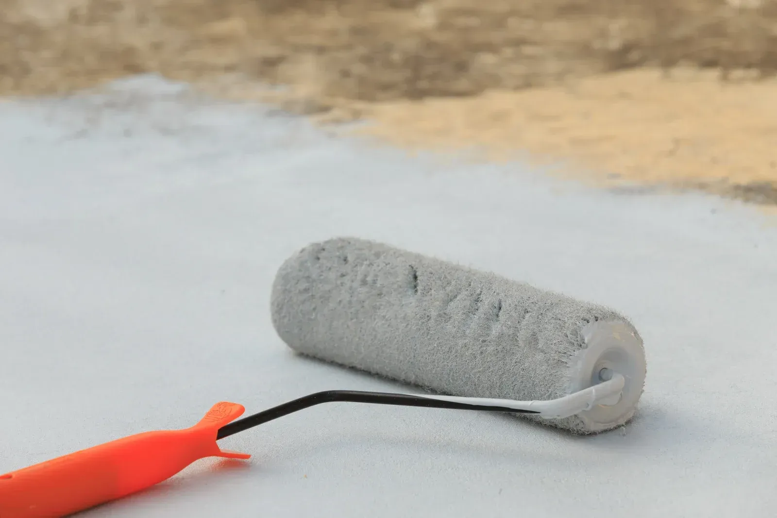 A paint roller is being used to paint a concrete surface.