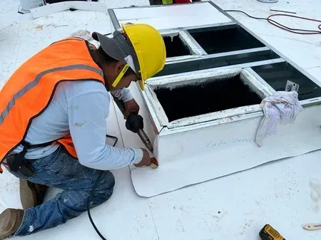 A man wearing a hard hat and safety vest is working on a roof.